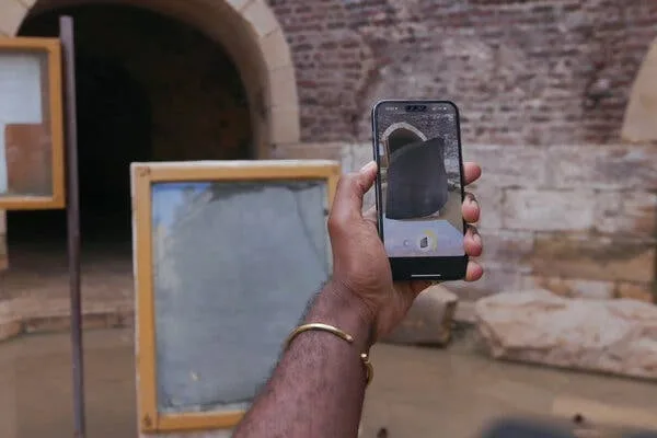 A man’s hand holds a cellphone on which a digital representation of the Rosetta Stone can be seen.