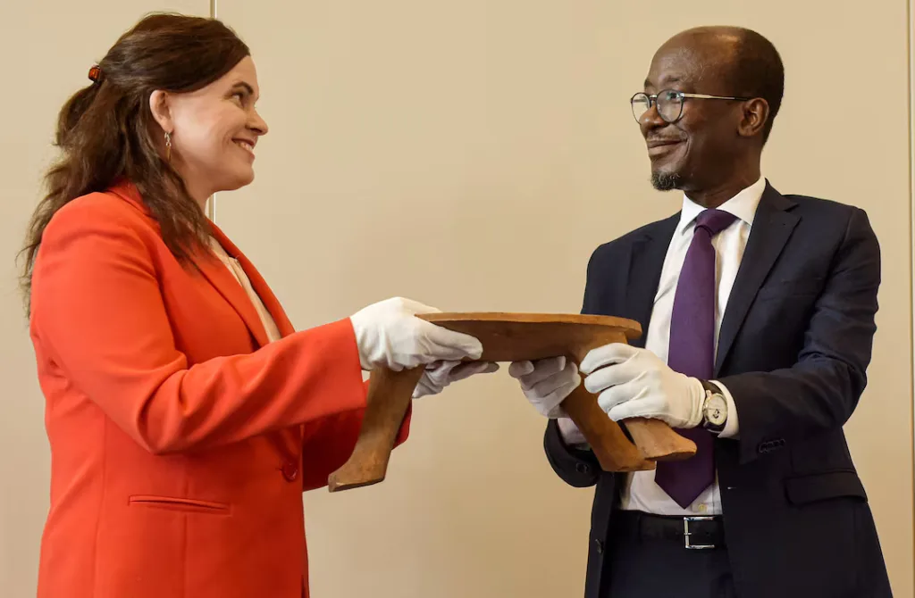 Finland’s Talvitie hands katakle stool to Benin’s Abimbola, May 13, 2025. (Image credits: REUTERS/Charles Placide Tossou)