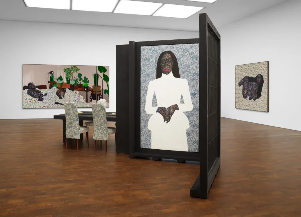 Art gallery with abstract portraits; a central panel depicts a figure in white with dark features. Surrounding walls display vibrant, plant-themed and textured art.