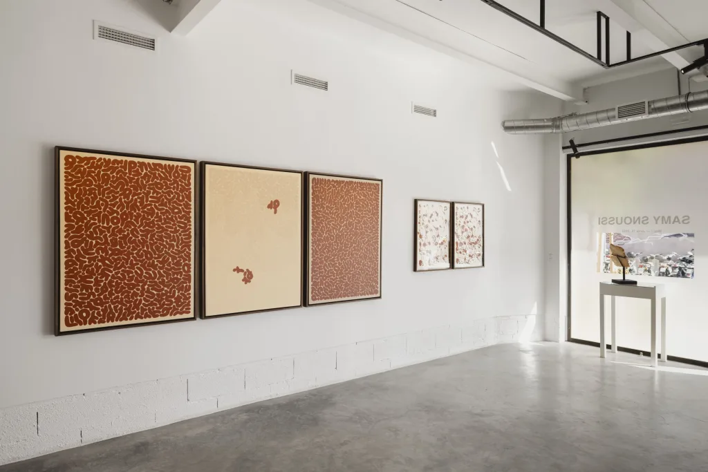 Art gallery with five abstract paintings in shades of brown and beige, featuring intricate patterns. Sunlit room with a minimalist, tranquil atmosphere.