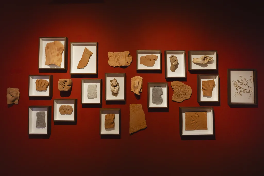 Framed clay tablets with imprints and textured patterns displayed on a red wall, creating a warm, historical, and artistic ambiance.