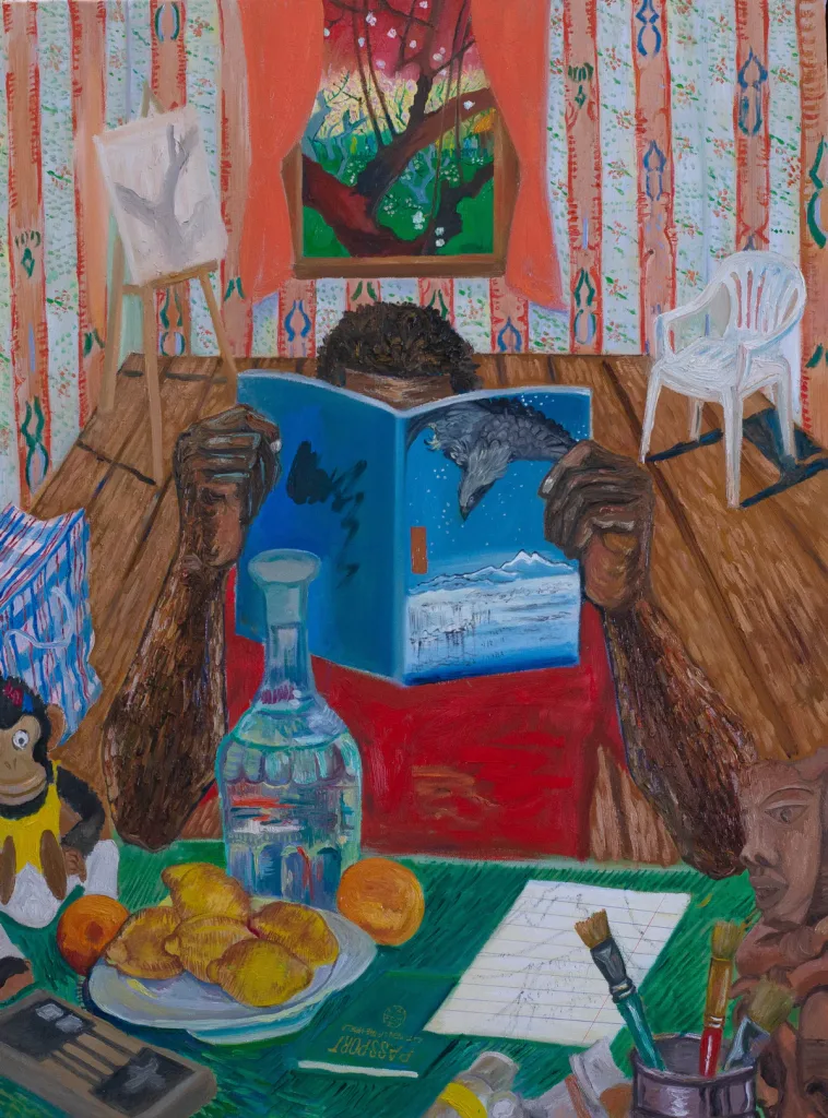 A person reads a bird-themed book in a vibrant room. The table is cluttered with a passport, snacks, a clear bottle, and paintbrushes. The window shows a colorful landscape, enhancing the cozy, artistic atmosphere.